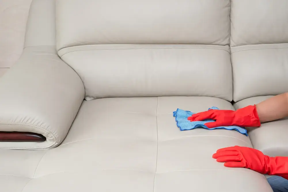 Cleaner wiping a light-coloured sofa with a microfibre cloth